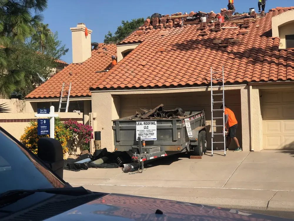 Leal Roofing crew re-roofing a red tile roof with the branded Leal Roofing trailer in the driveway in Scottsdale